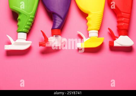 Bunte Sprühflaschen mit Reinigungsprodukten auf rosafarbenem Hintergrund, flache Lagen. Leerzeichen für Text Stockfoto