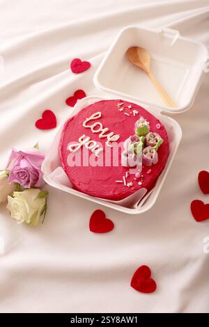 Romantischer roter Kuchen mit Liebesbotschaft und Rosen auf elegantem weißem Hintergrund Stockfoto