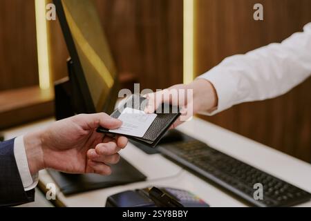 Mittlere Nahaufnahme einer nicht erkennbaren männlichen Hand, die seinen Pass und den Zimmerschlüssel nimmt Stockfoto