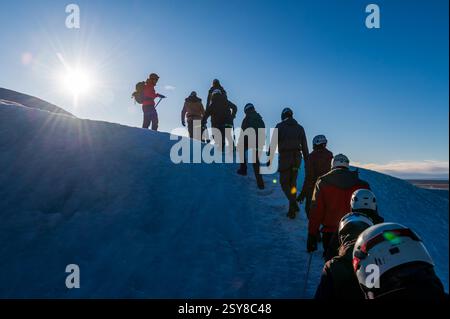 Eine Gruppe von Touristen, die sich alle zusammen aufhalten, um auf dem Vatnajokull-Gletscher in Island zu wandern, mit hellblauem Himmel Stockfoto