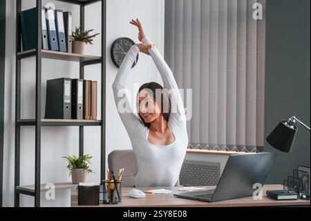 Macht eine Pause, streckt ihre Hände. Die junge schöne Frau in weißen Kleidern ist im Büro. Stockfoto