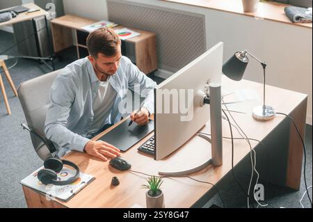 Draufsicht. Der Designer sitzt am Computer und verwendet ein Grafiktablett mit Stift. Stockfoto
