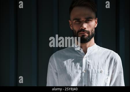Junger, gutaussehender Mann mit Bart und weißem Hemd steht vor dunkelgrünem Hintergrund. Stockfoto