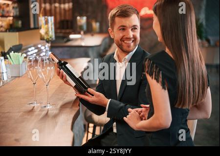 Lächelnd und mit einer Flasche Wein. Mann und Frau sitzen an der Bar mit Alkohol. Stockfoto
