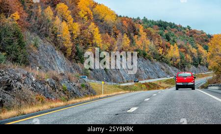 Ein roter Pickup-Truck fährt auf einer kurvenreichen Autobahn, umgeben von lebhaftem Herbstlaub. Stockfoto