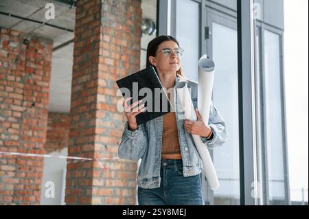 Die junge Frau steht im unfertigen Gebäude auf der Baustelle und arbeitet an einem Projekt. Stockfoto