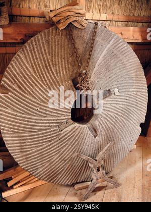 11. Januar 2025: Ede, Niederlande: Ein historischer Mühlstein mit seiner Scholle und Kette auf dem Steinboden der Windmühle Concordia, der die niederländische Mühle HE zeigt Stockfoto