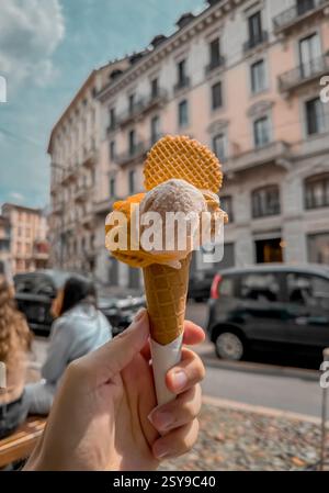 Eis in einem Kegel mit verschiedenen Aromen und Farben mit einem Löffel vor dem Hintergrund einer verschwommenen Stadt im Sommer im Urlaub. Hochwertiges Foto Stockfoto
