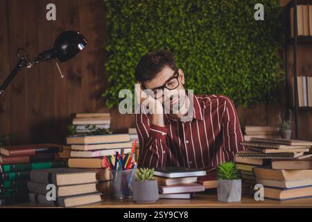 Junger Mann, der zu Hause studiert und von Büchern umgeben ist, während er sich auf eine Prüfung in einem gemütlichen und kreativen Innenarbeitsplatz vorbereitet. Stockfoto