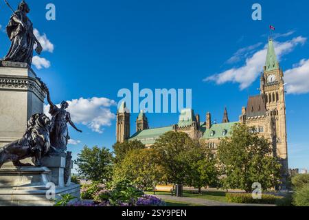 Großes Gebäude mit einem Uhrenturm und einer Statue einer Frau. Das Gebäude ist von Bäumen und Blumen umgeben Stockfoto