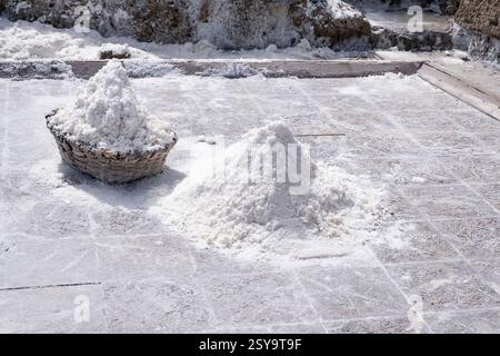 Ein großer Stapel frisch geernteten Salzes in einem Korb befindet sich neben einem Verdunstungsteich unter der Sonne, natürlicher Salzernteprozess, Salzhaufen in sal Stockfoto