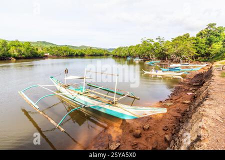 Mehrere Bancas liegen am Sandstrand mit üppigen grünen Hügeln und klarem Wasser im Hintergrund in Coron, Palawan, Philippinen Stockfoto