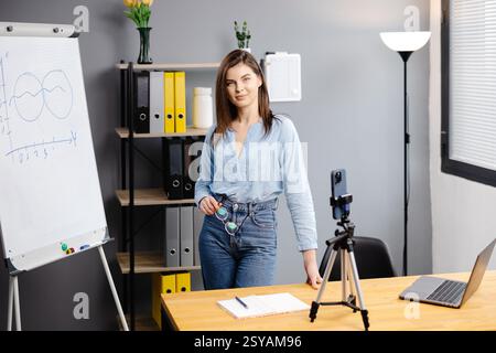 Junge Frau Mentorin nimmt Präsentationen auf, Webinar über Smartphone auf Stativ stehend, Lehrer Coach erklärt, hält Online-Unterricht, mit Telefon-Webc Stockfoto