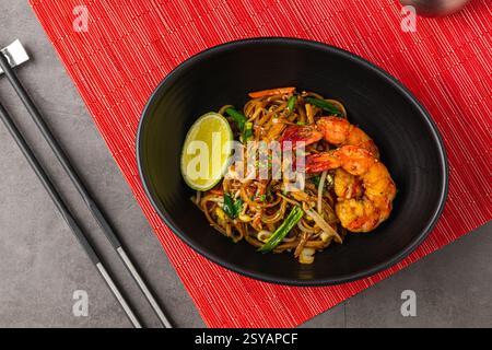 Blick von oben auf Shrimps Pad Thai mit Limette in einer schwarzen Schüssel Stockfoto