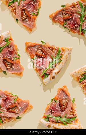 Blick von oben auf frisch gebackene Pizzascheiben mit Schinken, sonnengetrockneten Tomaten, Mozzarella, Rucola und geriebenem Parmesan, angeordnet in einem Muster auf Stockfoto