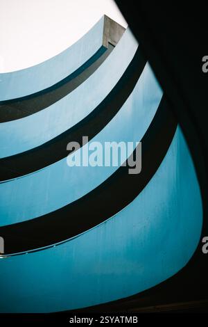 Architekturfoto eines blauen Parkhauses mit mehreren geschwungenen Schichten und einer dynamischen Perspektive. Das Bild erfasst den fließenden lin Stockfoto