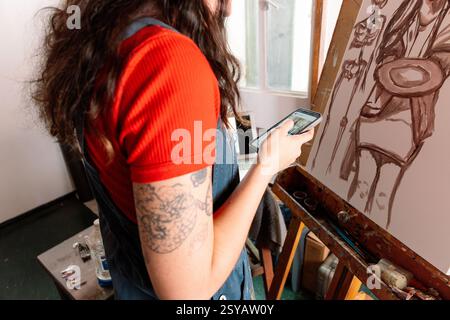Eine junge Frau malt eine Leinwand in ihrem Atelier, umgeben von Kunstgegenständen. Sie konzentriert sich intensiv auf ihre Arbeit, fängt Kreativität und Ausdruck ein Stockfoto