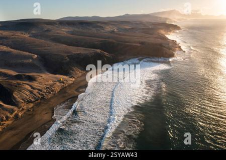 Ein atemberaubender Blick auf den Sonnenuntergang über der ruhigen Küste von Riscos La Pared auf Fuerteventura, der das goldene Licht auf dem wilden Gelände einfängt Stockfoto