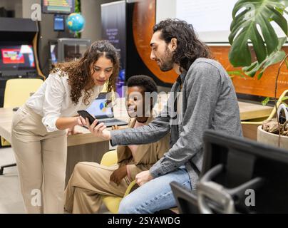 In einem modernen Büro arbeitet eine Gruppe von Fachleuten zusammen und diskutiert Informationen, die auf einem Smartphone angezeigt werden. Das Ambiente spiegelt Teamwork wider, inn Stockfoto
