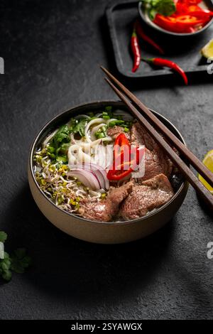 Eine Schüssel vietnamesisches Rindfleisch Pho Nudelsuppe (Pho Bo) mit Scheiben zartem Rindfleisch, Reisnudeln, frischen Kräutern und lebendigem Gemüse, herrlich arr Stockfoto