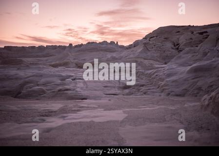 Ätherischer Sonnenuntergang mit Blick auf die einzigartigen Felsformationen von Sarakiniko auf der Insel Milos, Griechenland, unter einem pastellfarbenen Himmel. Stockfoto