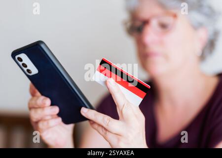 Eine Seniorin hat ein Smartphone und eine Kreditkarte, die Online-Shoppingaktivitäten macht. Das Bild zeigt den wachsenden Trend digitaler Transaktionen unter Stockfoto