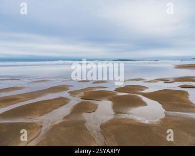 Ruhige Küstenlandschaft mit ausgedehnten Sandstränden und reflektierenden Gezeitenbecken unter bewölktem Himmel, die die Schönheit und Ruhe der Natur vermitteln. Stockfoto