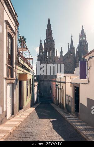 Dieses Bild fängt die atemberaubende Kirche San Juan Bautista in Arucas, Gran Canaria, ein, von einer malerischen, engen Straße, gesäumt von farbenfrohen Tram Stockfoto
