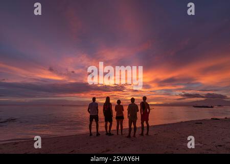 Rückansicht Silhouette von nicht erkennbaren Freunden, die an einem Strand auf den Philippinen stehen und einen atemberaubenden Sonnenuntergang mit leuchtenden Farben am Himmel beobachten. Idee Stockfoto