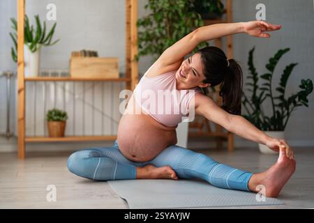 Eine sportlich schwangere Frau in aktiver Kleidung macht Übungen auf Yogamatten. Stockfoto