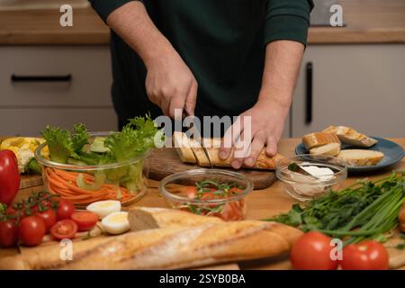 Frisches Brot mit Händen in buntem Gemüse wie Salat, Karotten und Tomaten schneiden. Eine gesunde Zubereitungsszene betont gesunde Ernährung und Stockfoto