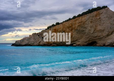 Kristallklares türkisfarbenes Wasser ragt sanft an die Küste des Strands Porto Katsiki in Lefkada, Griechenland, eingerahmt von dramatischen Klippen und einem bewölkten Himmel. Stockfoto