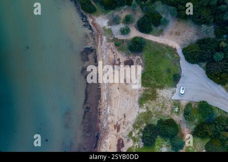 Von oben aus blickt man auf einen Wohnmobil, der in der Nähe des wilden Strandes Marathias parkt, umgeben von natürlichem Grün und einer zerklüfteten Küste mit ruhigem, flachem Wasser Stockfoto