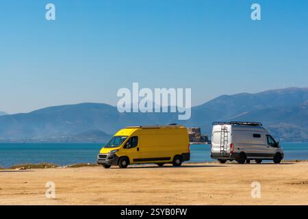 Zwei Wohnmobile parkten am Strand Arvanitias in Nafplion, Griechenland, mit der Festung Palamidi auf dem Berg im Hintergrund. Ein perfekter Ort für Van l Stockfoto