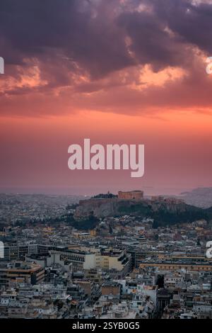 Ein atemberaubender Blick auf Athen bei Sonnenuntergang mit dem Parthenon und der Akropolis, die vor einem dramatischen Himmel beleuchtet werden. Das Stadtbild erstreckt sich bis zum h Stockfoto