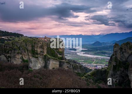 Fesselnder Blick auf den Sonnenuntergang des historischen Klosters der Heiligen Dreifaltigkeit, das auf den hohen Klippen Griechenlands thront, mit einem ruhigen Tal und weit entfernten, schneebedeckten pe Stockfoto