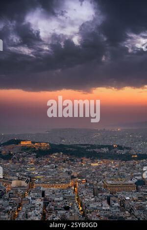 Ein dramatischer Sonnenuntergang über Athen, Griechenland, mit dem Parthenon und der Akropolis auf dem Hügel beleuchtet. Die Lichter der Stadt erwachen allmählich, während dunkle Wolken auftauchen Stockfoto