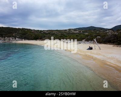 Ein friedlicher Blick aus der Luft auf den wilden Strand von Kalamitsi in Griechenland. Ein Paar sitzt auf dem goldenen Sand von türkisfarbenem Wasser, umgeben von üppigem Grün und einer ruhigen Atmosphäre Stockfoto