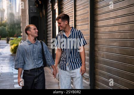 Ein schwules Paar macht einen gemütlichen Spaziergang, Hand in Hand, durch die pulsierenden Straßen Madrids. Ihr Lächeln spiegelt Freude und Akzeptanz wider, symbolisiert Liebe und Stockfoto