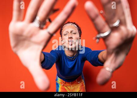 Eine modische Frau hebt sich in einer lebendigen Hose hervor, die auf spielerische Weise ein Fischgesicht zaubert. Sie zeigt eklektischen Schmuck und ein auffälliges blaues Oberteil gegen ein helles Stockfoto