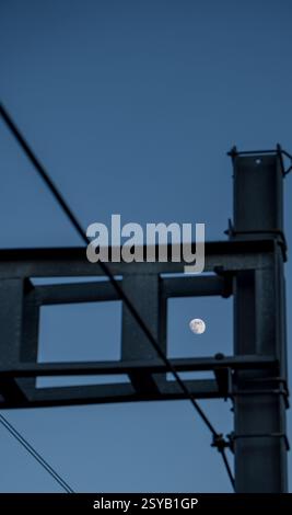 Der Vollmond ist perfekt in einer geometrischen Metallstruktur eingerahmt und schafft einen markanten Kontrast zwischen Natur und Industrie. Der tiefblaue Himmel enha Stockfoto