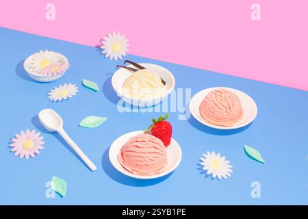 Eine einladende Präsentation von Eiskugeln in weißen Schüsseln vor einem leuchtend blau-rosa geteilten Hintergrund. Die Szene wird mit verspielten Gänseblümchen und verfeinert Stockfoto