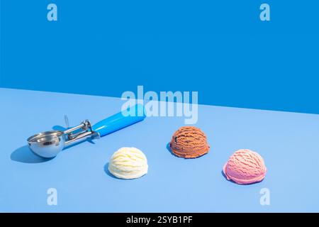 Drei Kugeln Eis in Schokolade, Erdbeere und Vanille auf einem leuchtend hellblauen und blauen Hintergrund, begleitet von einem blau gestreiften M Stockfoto