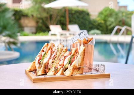 Eine köstliche Platte mit Schinken, Käse und Tomaten-Sandwich, serviert mit knusprigen Pommes frites in einem Korb. Die Lage ist ruhig, am Pool, der Entspannung weckt Stockfoto