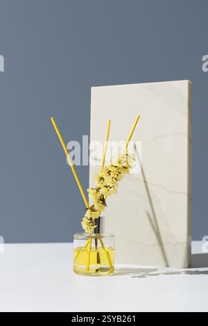 Eleganter Glasdiffusor mit gelbem Schilf, der einen frischen Zitronenduft verströmt. Ergänzt durch zarte getrocknete Blüten. Perfekt für Wohnkultur und Aromatherapie Stockfoto