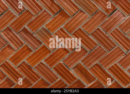Ziegelwand mit klassischem Fischgrätenmuster. Die rot gefärbten Steine sind diagonal angeordnet und erzeugen einen dynamischen visuellen Effekt. Perfekt für Backgr Stockfoto