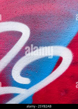 Eine Nahaufnahme lebendiger Graffiti-Kunstwerke mit roten, blauen und weißen Farben auf einer strukturierten Wand. Die abstrakten, geschwungenen Formen und die auffälligen Kontraste bilden cre Stockfoto