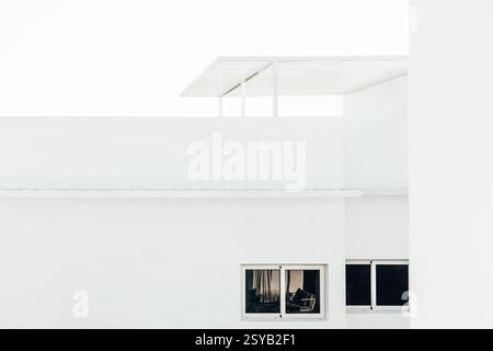 Ein modernes minimalistisches Architekturdesign mit einem weißen Gebäude mit scharfen klaren Linien, großen Fenstern und einer eleganten Pergola. Stockfoto