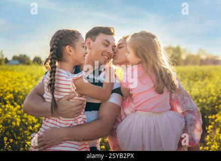 Ein Vater mit seiner Frau und zwei Töchtern, die ihn in einem sonnendurchfluteten Blumenfeld mit Liebe duschen. Diese berührende Szene fängt Familienbeziehungen ein, wa Stockfoto