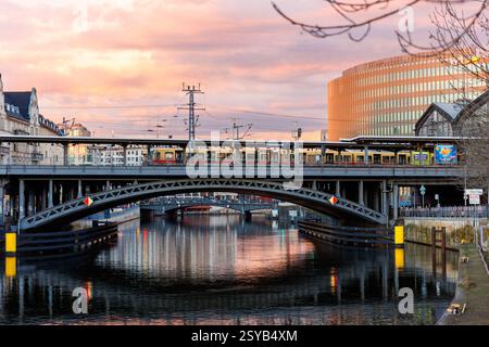 Berlin, Deutschland - 25. Februar 2024: Panoramablick Berliner Bahnhof Friedrichstraße DB-Zug überquert eine Metallbrücke vor dem dramatisch warmen Sonnenuntergangshimmel. Abends Stockfoto